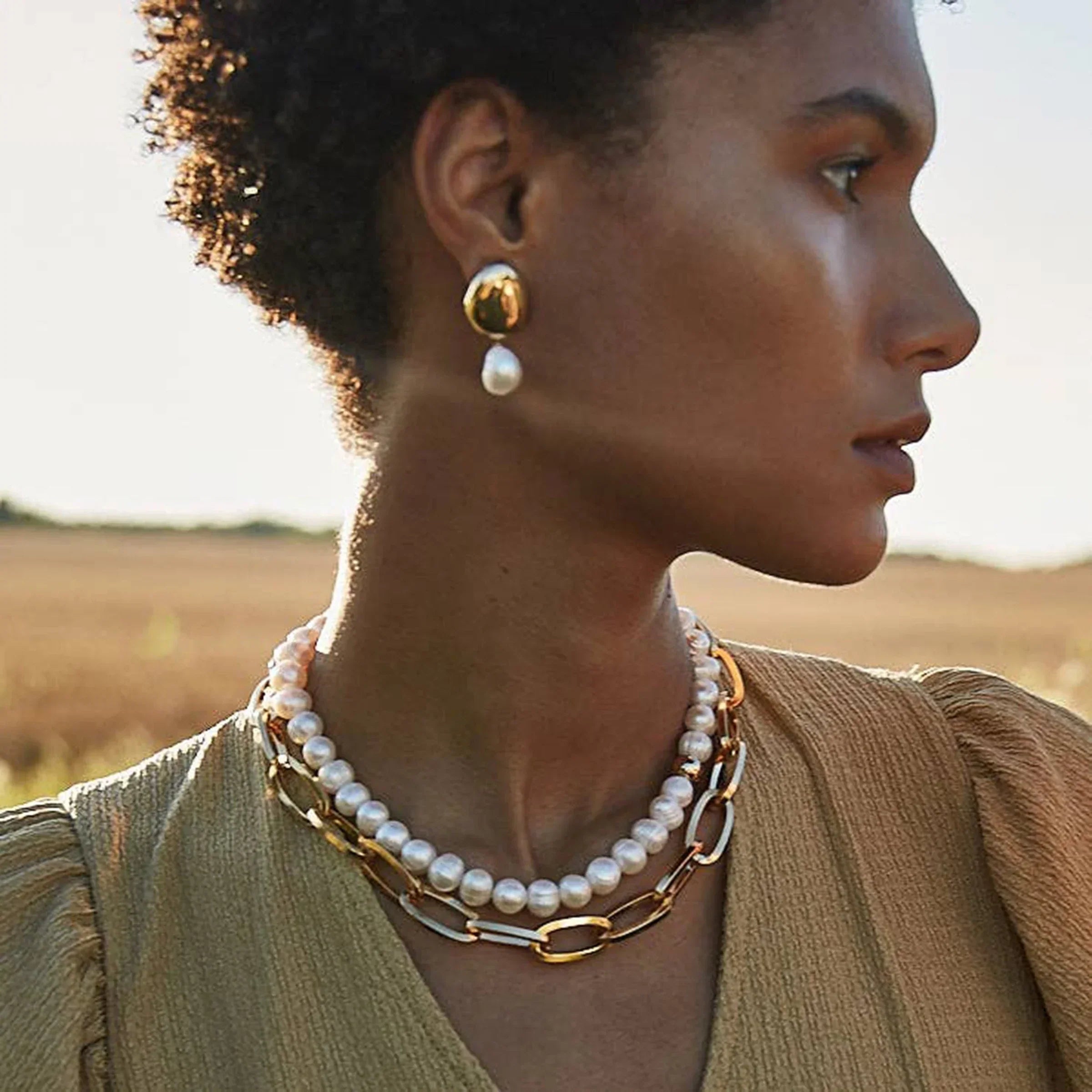 Essential Chainlink Gold Collar on a model wearing a khaki green short sleeve v-neck and the image is a close up of necklace paired with chunky pearls..