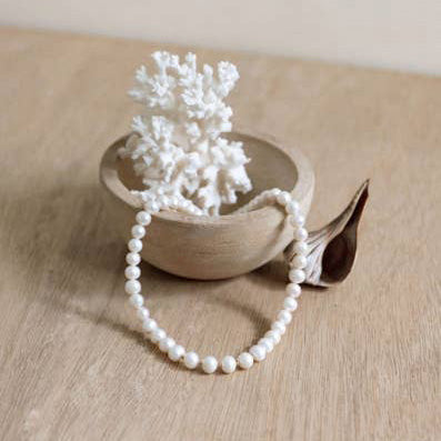 A pearl bracelet laying in a ceramic dish holding a white sea coral on a natural hued table