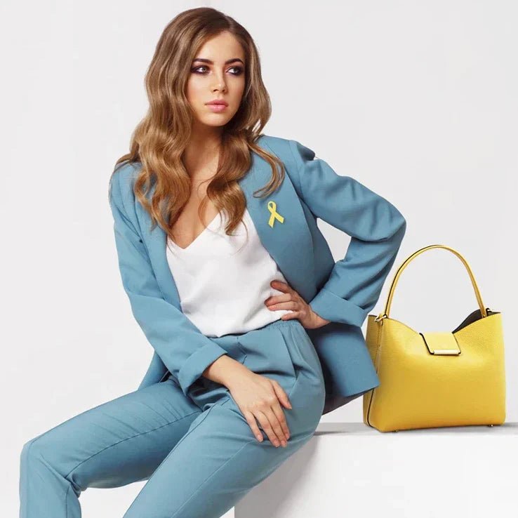 Female model with long blonde wavy hair and wearing a light blue pant suit is sitting next to the  Pebbled Leather Secchiello Bag in Pastel Yellow showing front of bag