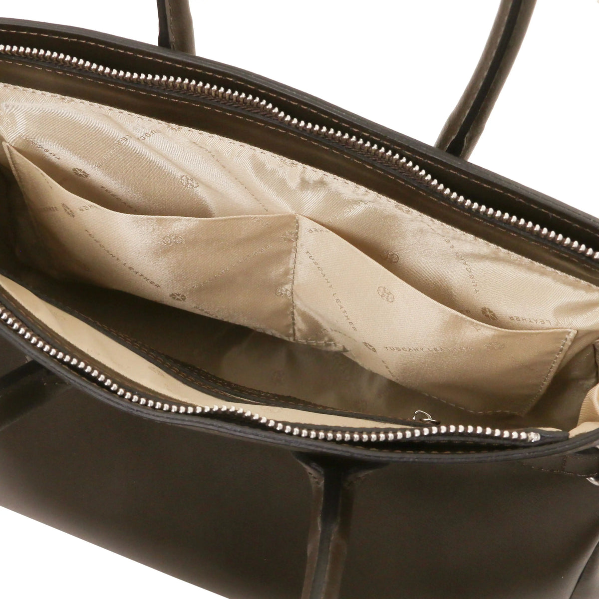 Close-up of the open interior of a chocolate leather handbag, showing a beige satin-lined compartment with stitched open pockets and silver-tone zipper trim.