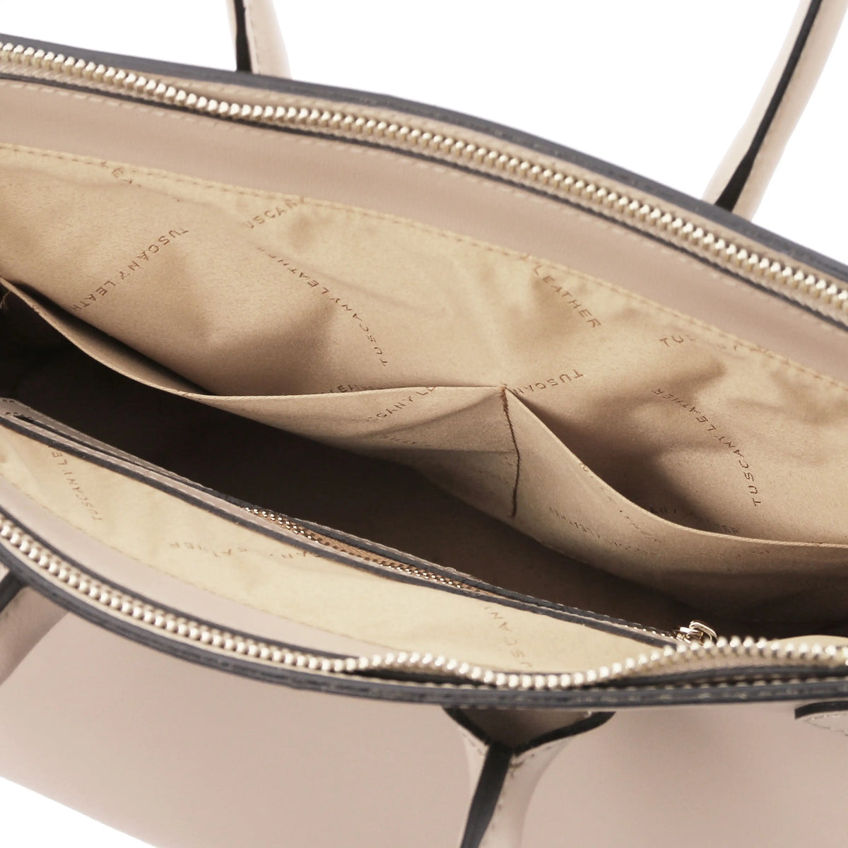 Close-up of the interior of a handbag showing a beige fabric lining with a repeating brand print, gold-tone zippers, open pockers and a light neutral exterior edge.