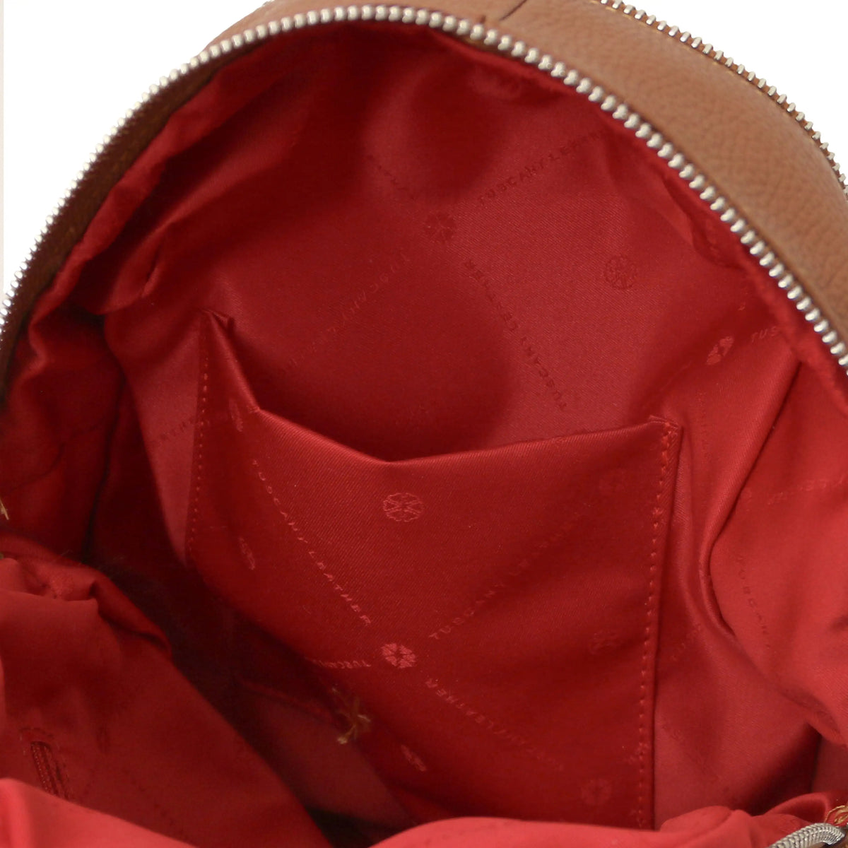 Close-up of the interior of a cognac leather backpack showing a red satin-lined pocket and a tan leather zipper trim with silver metal teeth.