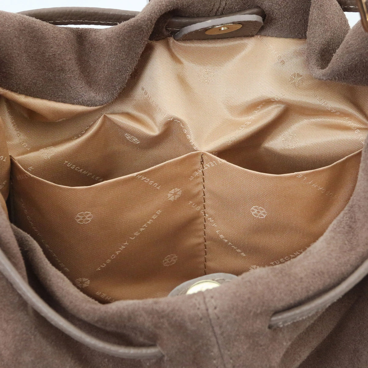 Close-up of the interior of a dark taupe suede shopper bag, showing a beige satin lining with a front pocket and the brand name 'Tuscany Leather' printed on liming.