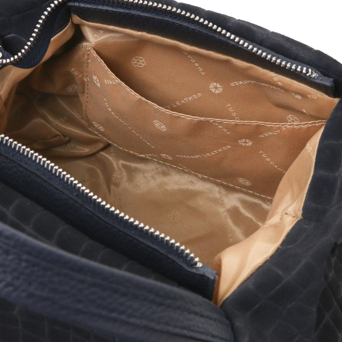 Close-up open pocket view of the interior of a dark blue croc print shoulder bag, with natural lining.