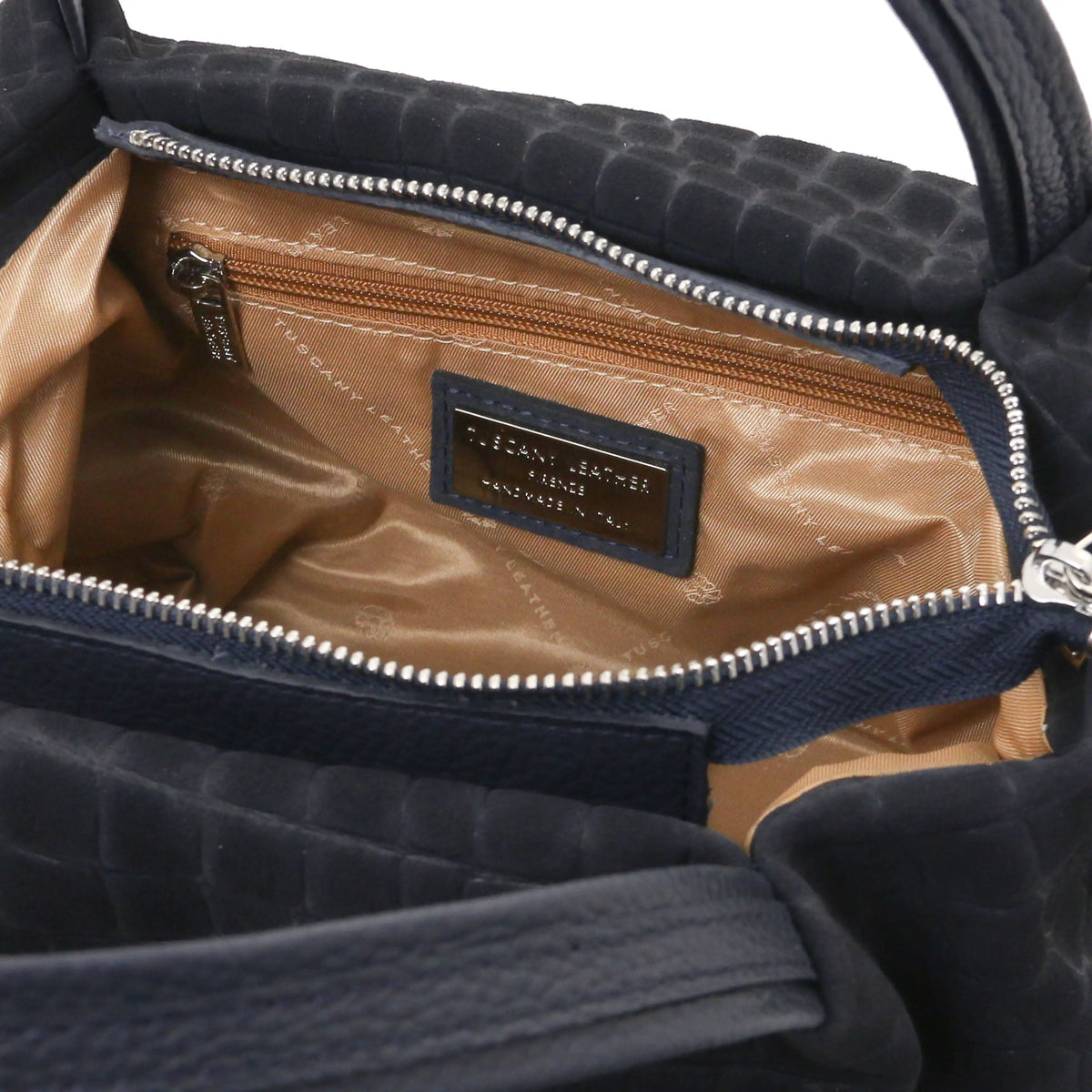 Close-up zip pocket view of the interior of a dark blue croc print shoulder bag, with natural lining small metal brand plaque.