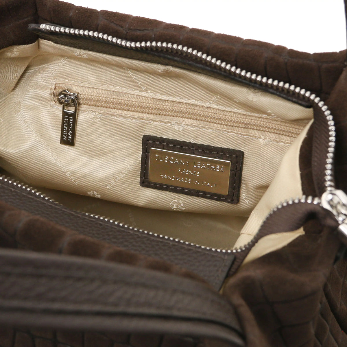 Close-up zip pocket view of the interior of a chocolate croc print shoulder bag, with beige lining small metal brand plaque.