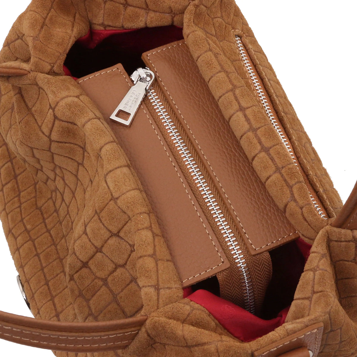 Close-up of a cognac textured handbag interior showing a zippered compartment, silver zipper pulls, and a red lining.