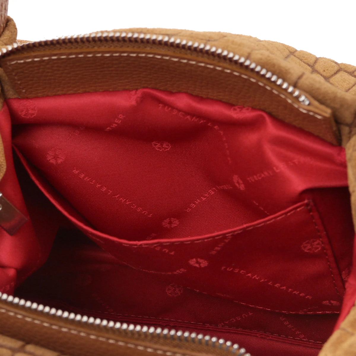Close-up open pocket view of the interior of a cognac croc print leather bag, showing a bright red lining with 'TUSCANY LEATHER' printed branding,