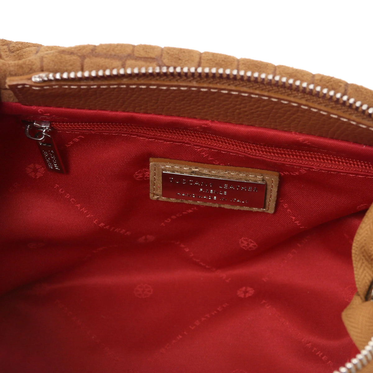 Close-up zip pocket view of the interior of a cognac croc print shoulder bag, with red  lining small metal brand plaque.