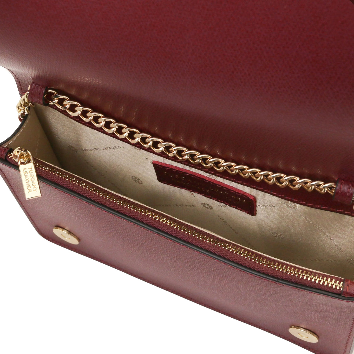 Close-up of a bordeaux leather clutch bag with a gold chain strap, gold zipper, and a beige interior lining.