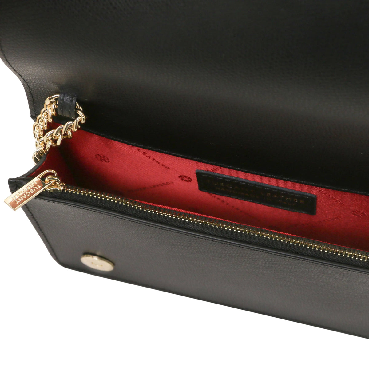 Close-up of a black leather clutch bag showing the interior red lining, gold-tone chain strap, and a black brand label inside.
