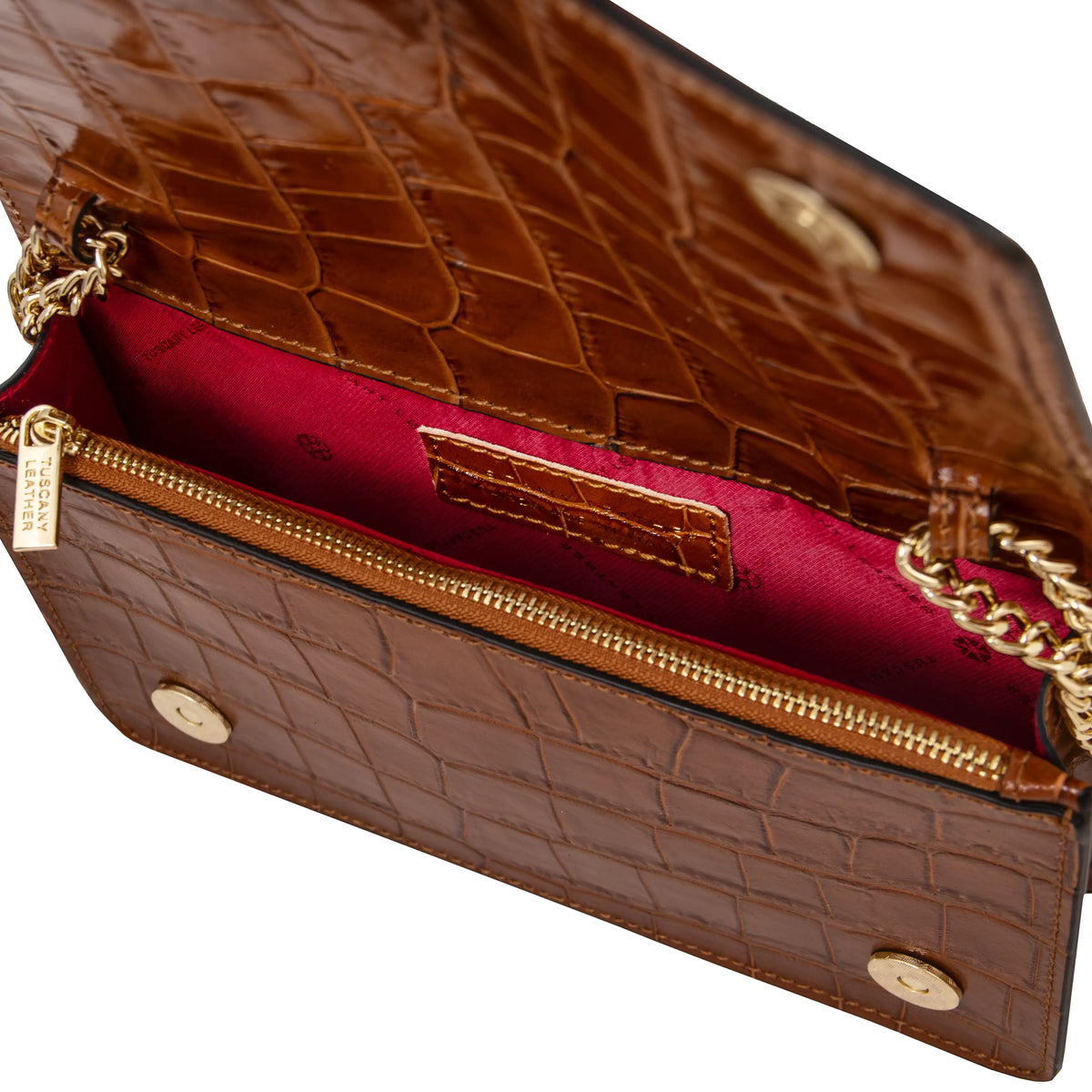 Close-up of a cognac crocodile-embossed leather handbag showing the red interior with a gold zippered compartment, gold chain strap, and beige lining. 