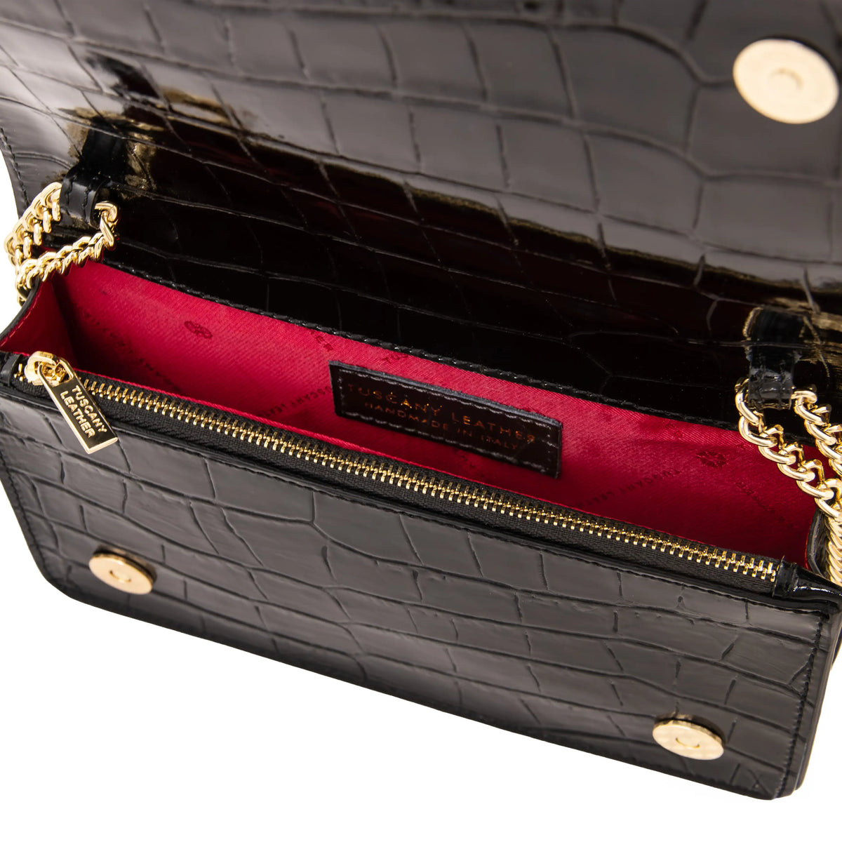 Close-up of a black crocodile-embossed leather handbag showing the interior with a bright red lining, gold-tone chain strap, zippered compartment, and hardware.