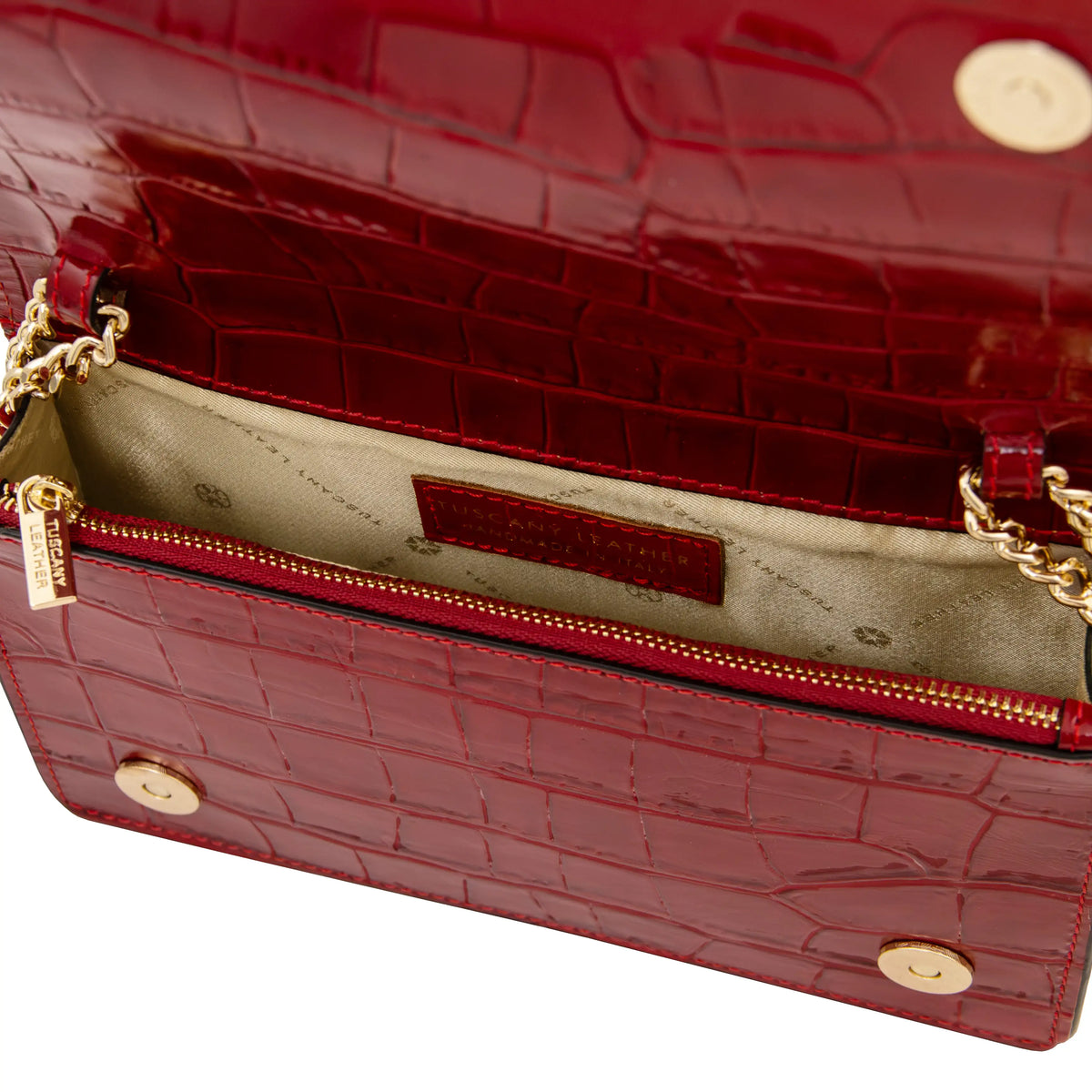 Close-up of a red crocodile-embossed leather handbag showing the interior with a gold zippered compartment, gold chain strap, and beige lining. 