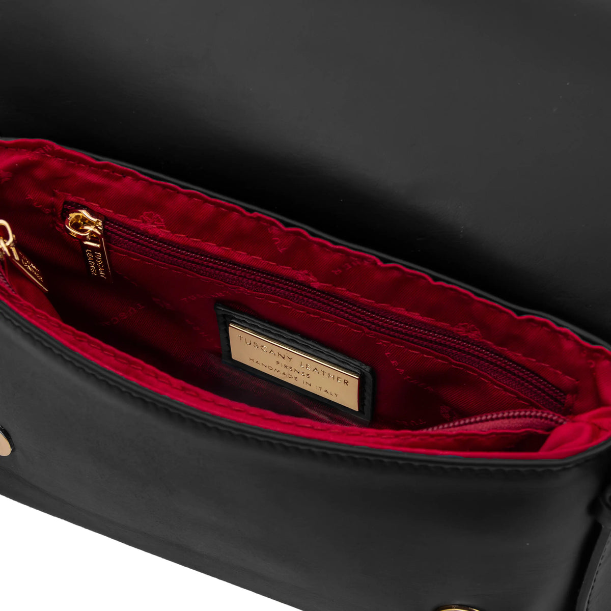 Close-up of a black leather handbag interior showing a deep red lining, zippered pocket, gold-tone hardware and a brand plaque.