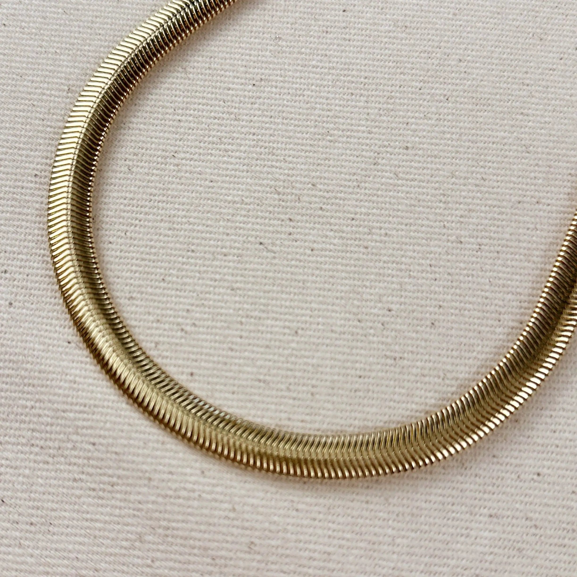 Gold snake necklaces on a textured beige background
