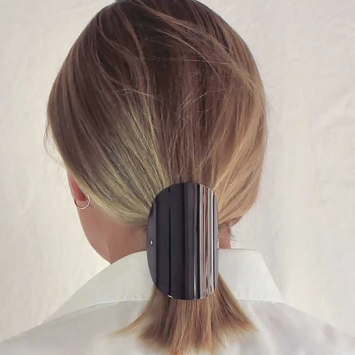 A close-up back view of a person with light brown hair wearing a large, wide oval black pony tail barrette.