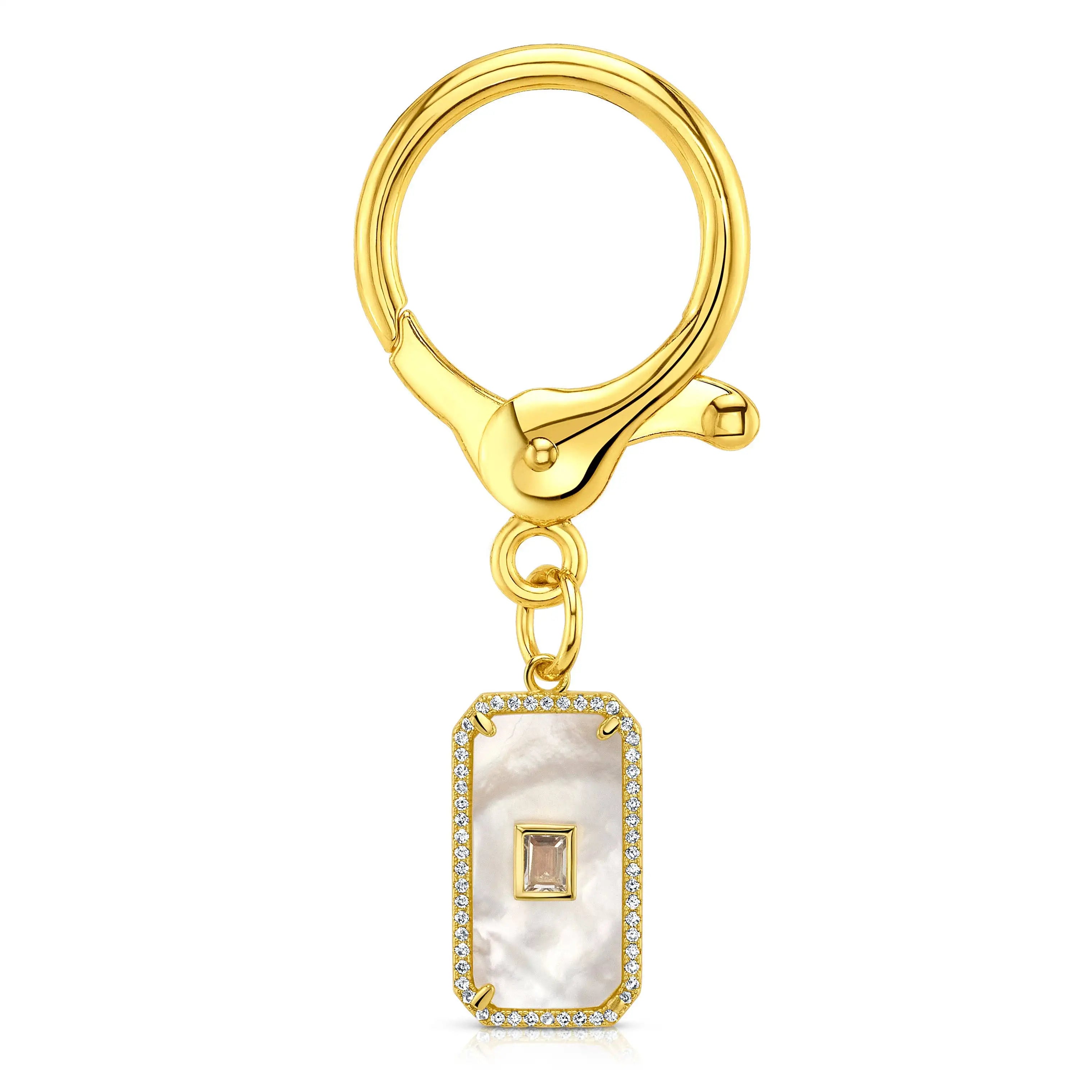 A gold-tone key ring with a rectangular pendant featuring a white mother-of-pearl inlay, a small square gold stone in the center, and a border of clear CZ crystals, shown on a plain white background.