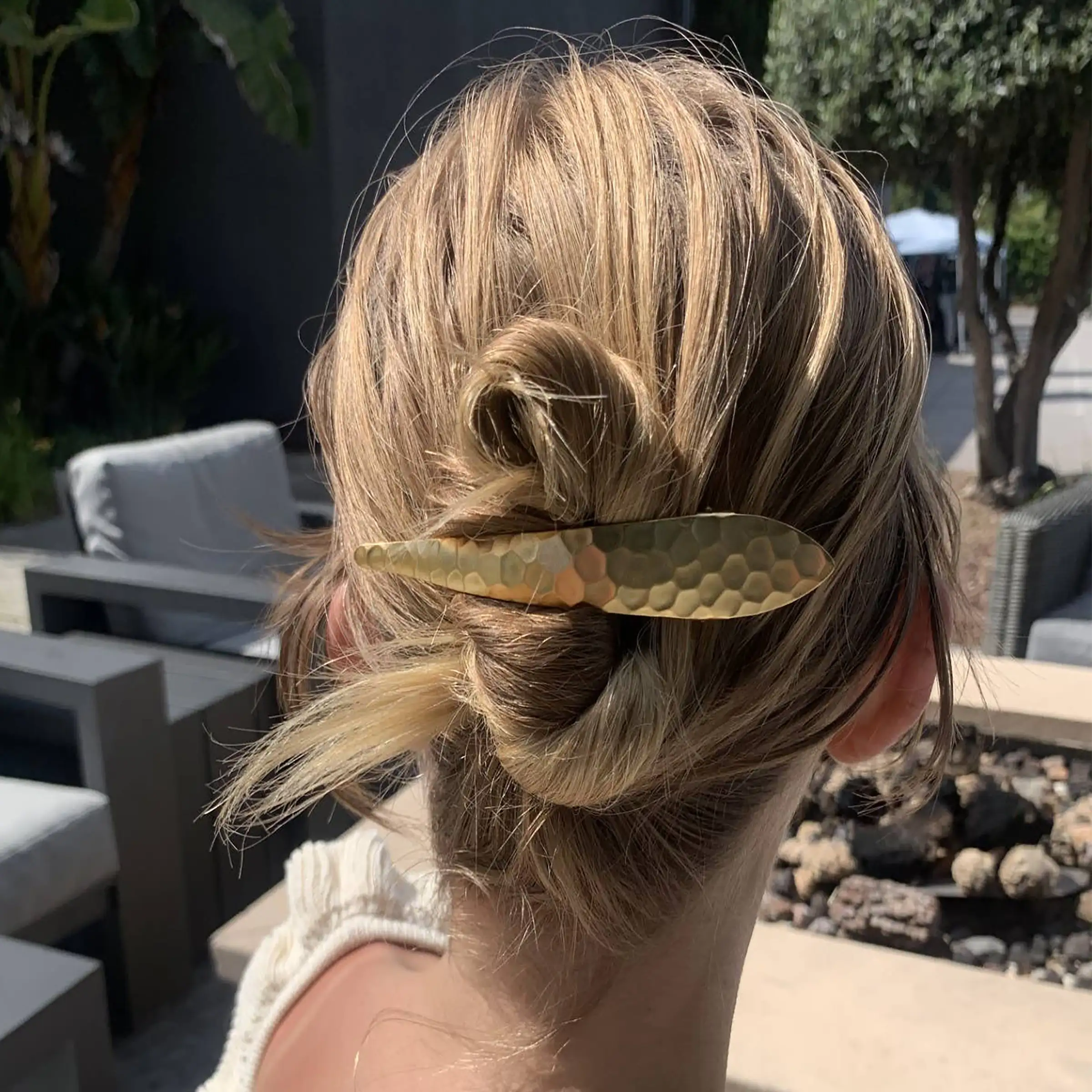 A woman with blonde hair styled in an updo wearing a gold hair hammered hair clip outdoors.