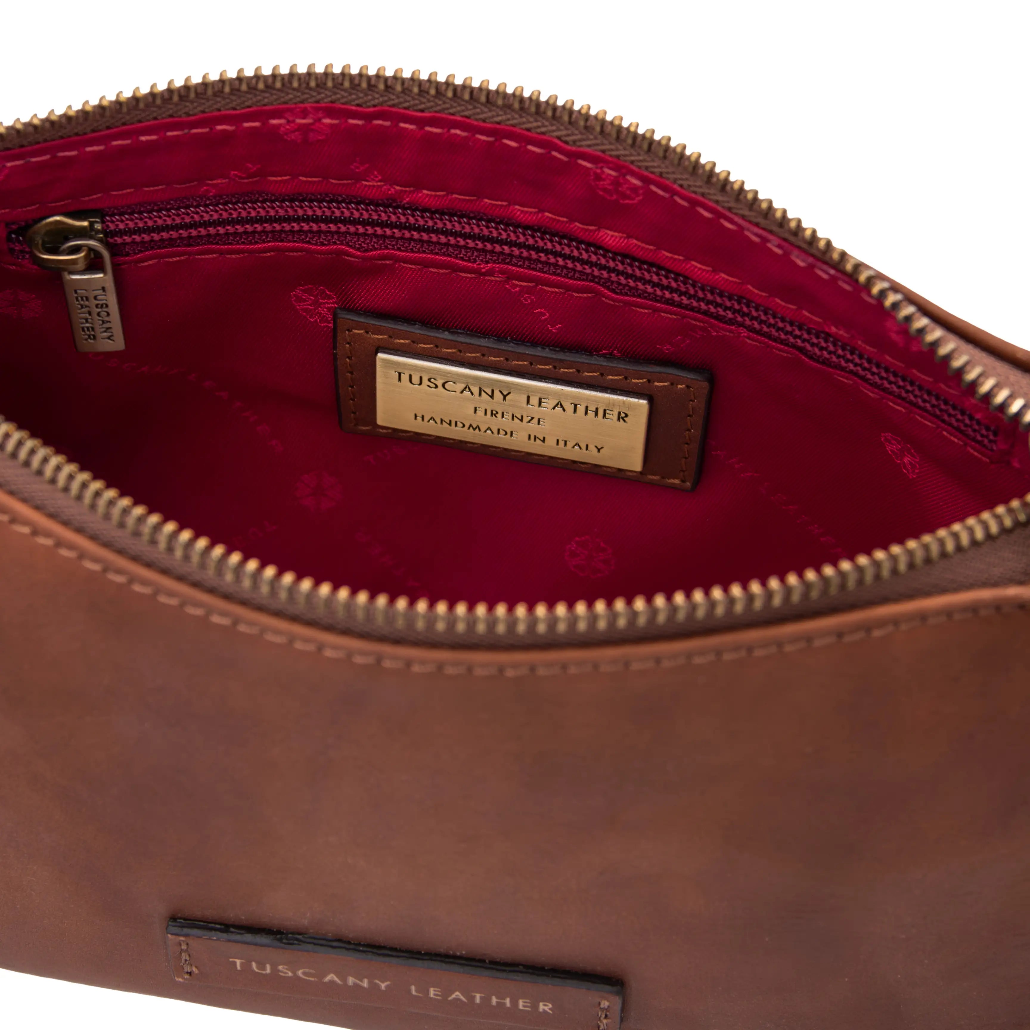 Brown leather bag with open zipper showing red interior and Tuscany Leather label.