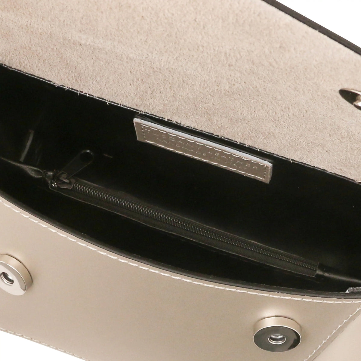 Close-up of a champagne gold  leather handbag interior showing a black zippered pocket with a silver-tone metal label and a suede-like lining.