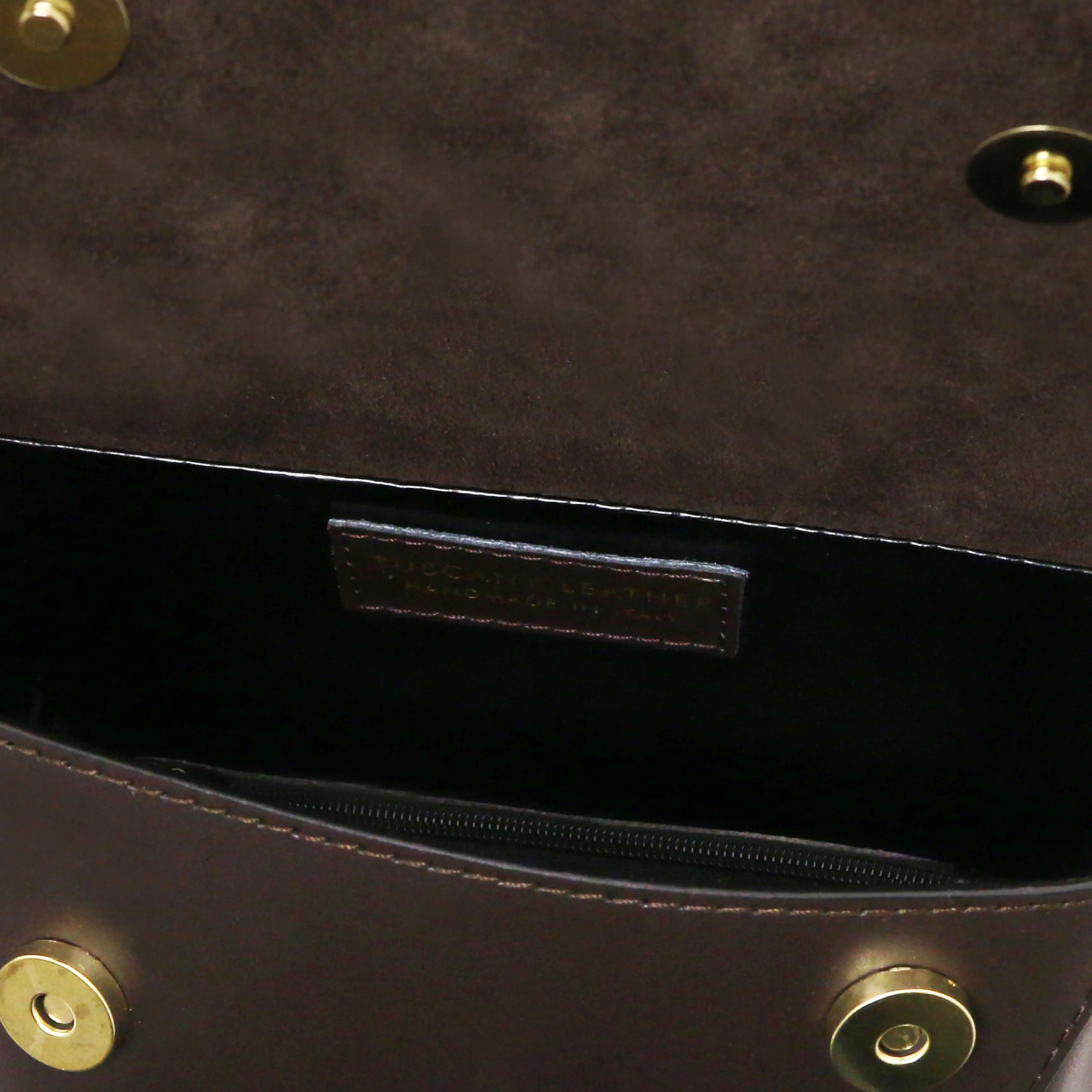 Close-up of a chocolate  leather handbag interior showing a black zippered pocket and brass-tone hardware.