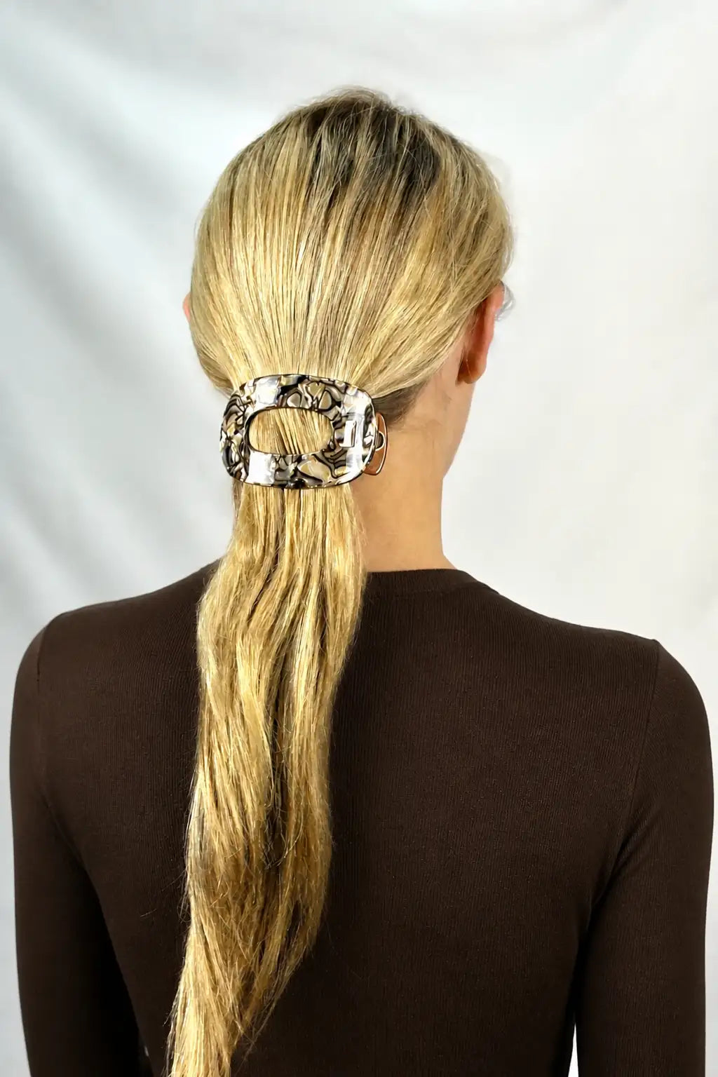 A woman viewed from the back wearing a brown swirl pattern flat hair claw clip holding her blonde ponytail. 