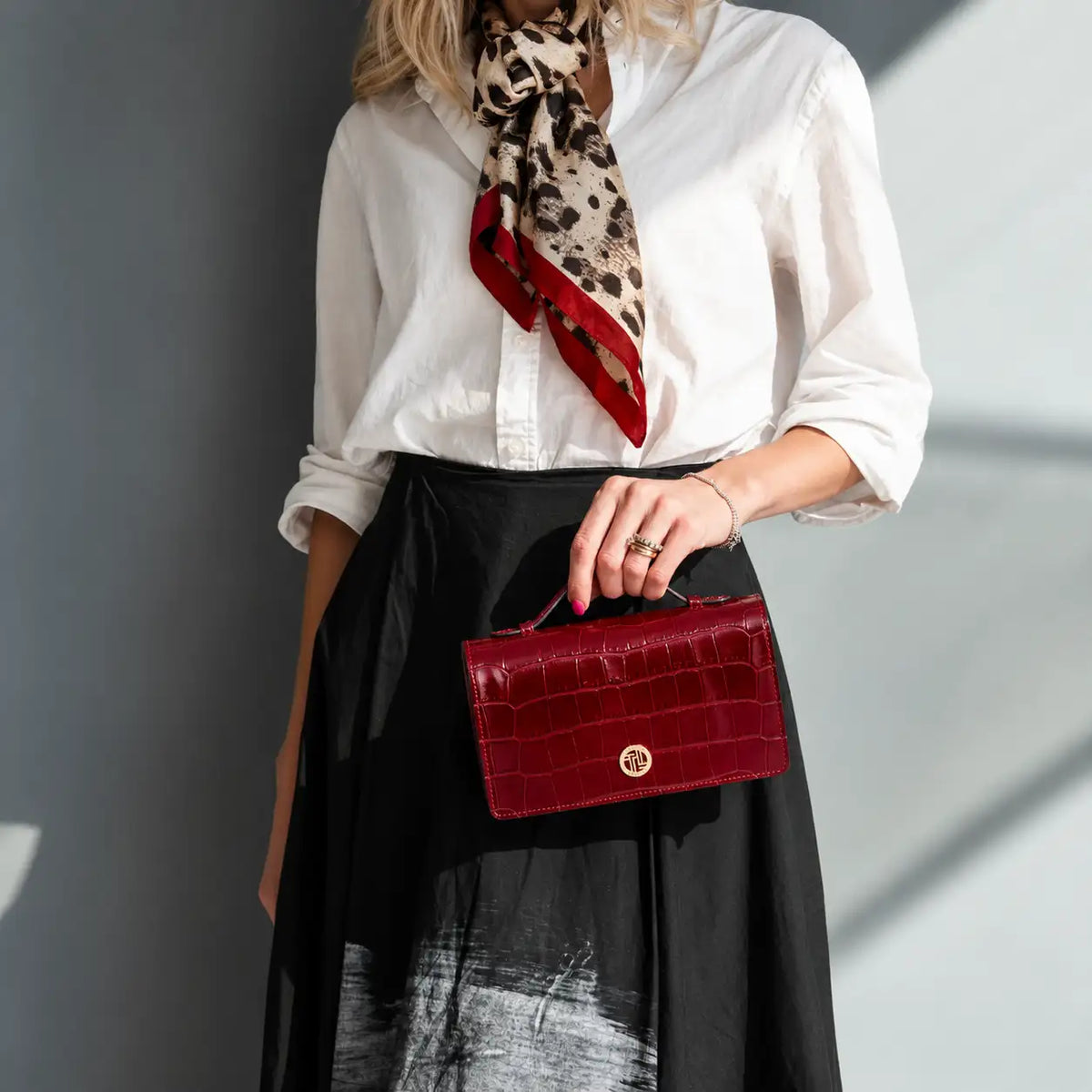 A woman wearing a white blouse, black skirt and leopard-print scarf carries a red crocodile-embossed shoulder bag sa a clutch.