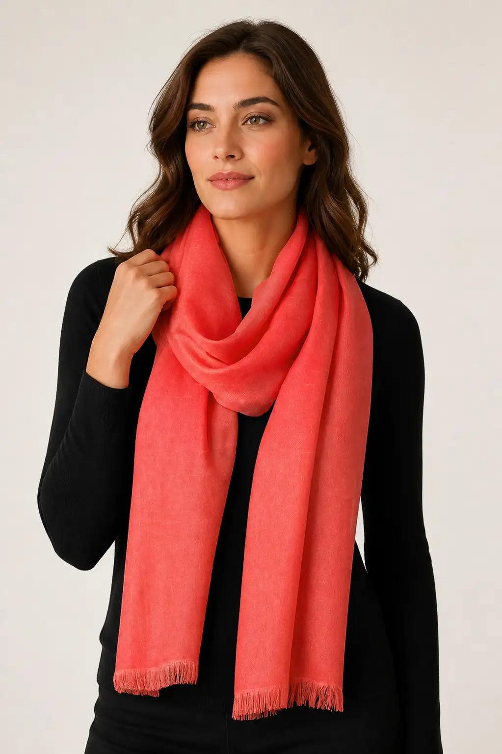 A woman with brown hair wearing a black long-sleeve top and a coral pink scarf, photographed against a light gray studio background.