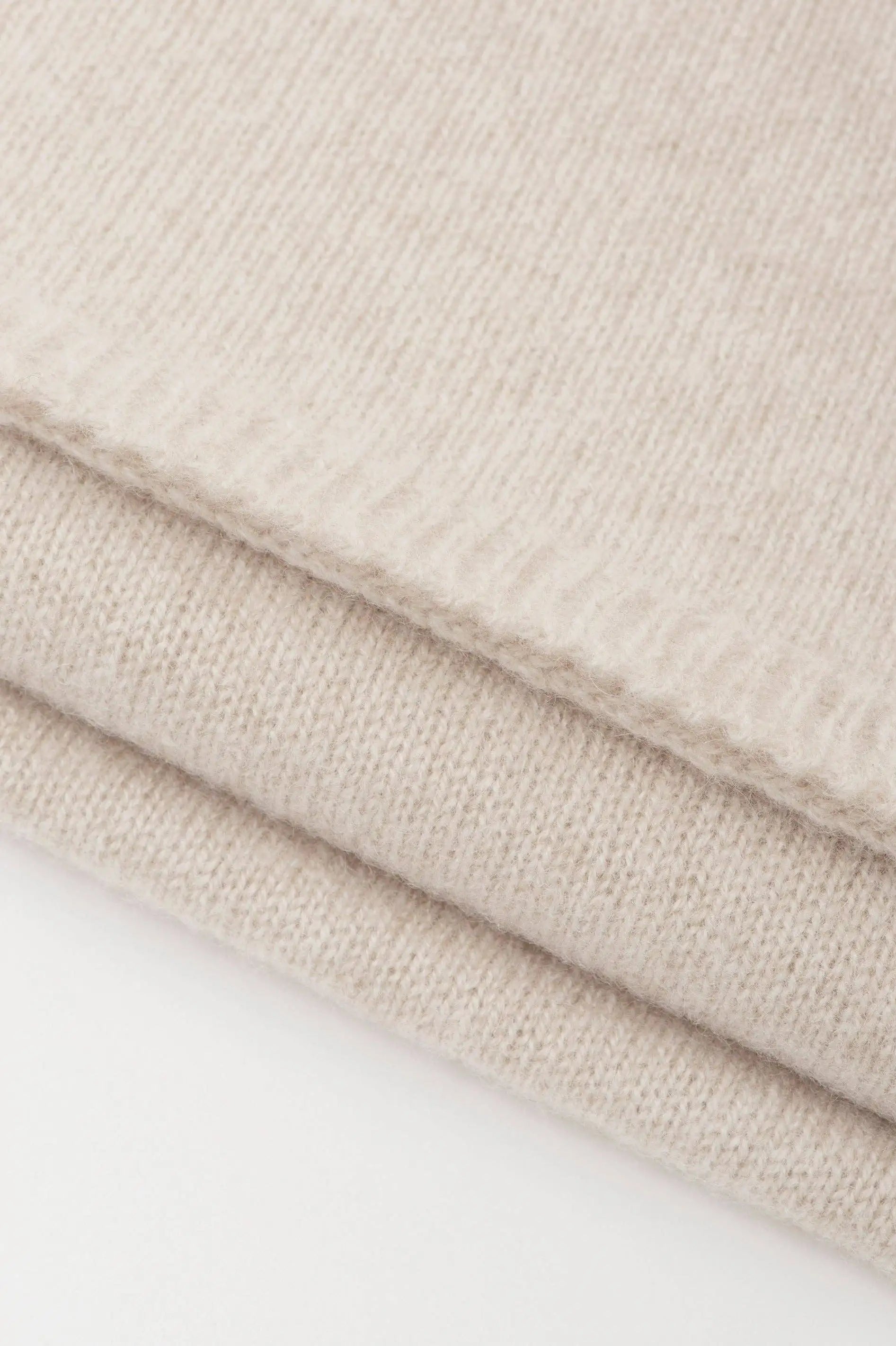 Close-up of folded knit fabric in a warm beige tone, showing the texture and ribbed edge.