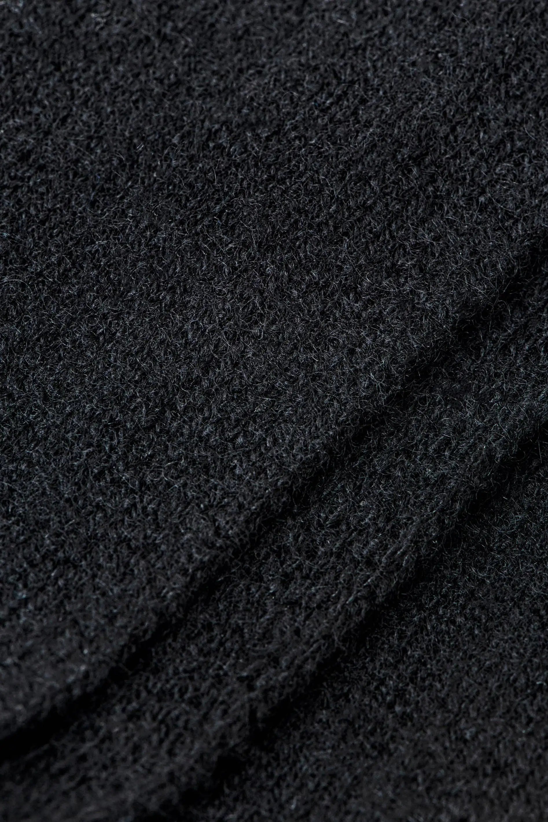 A close-up of a black textured knit fabric with soft folds.
