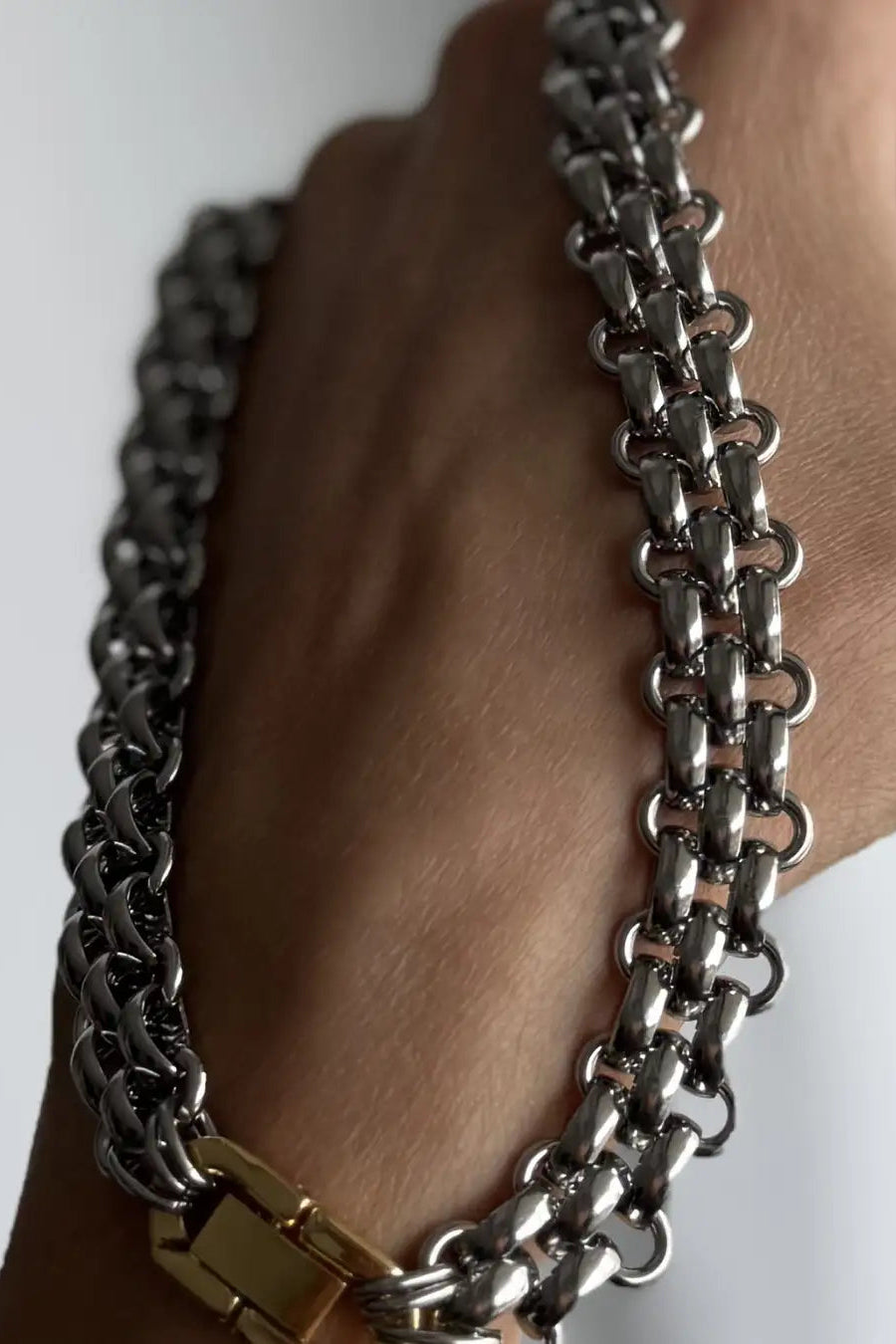 A close-up of a hand holding a thick, polished silver-toned chain bracelet with a gold-toned clasp, set against a plain light background.