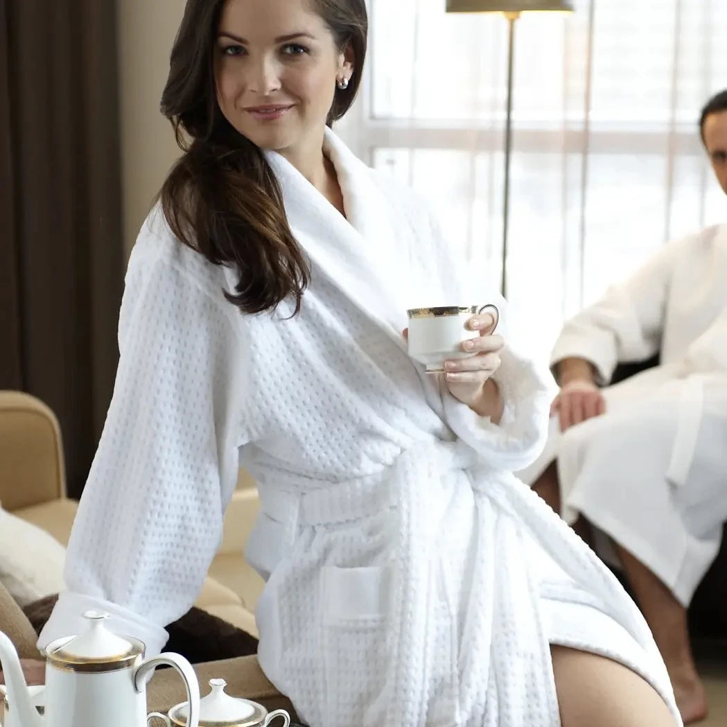 A woman is sitting holding a coffee cup wearing a white waffled knit robe