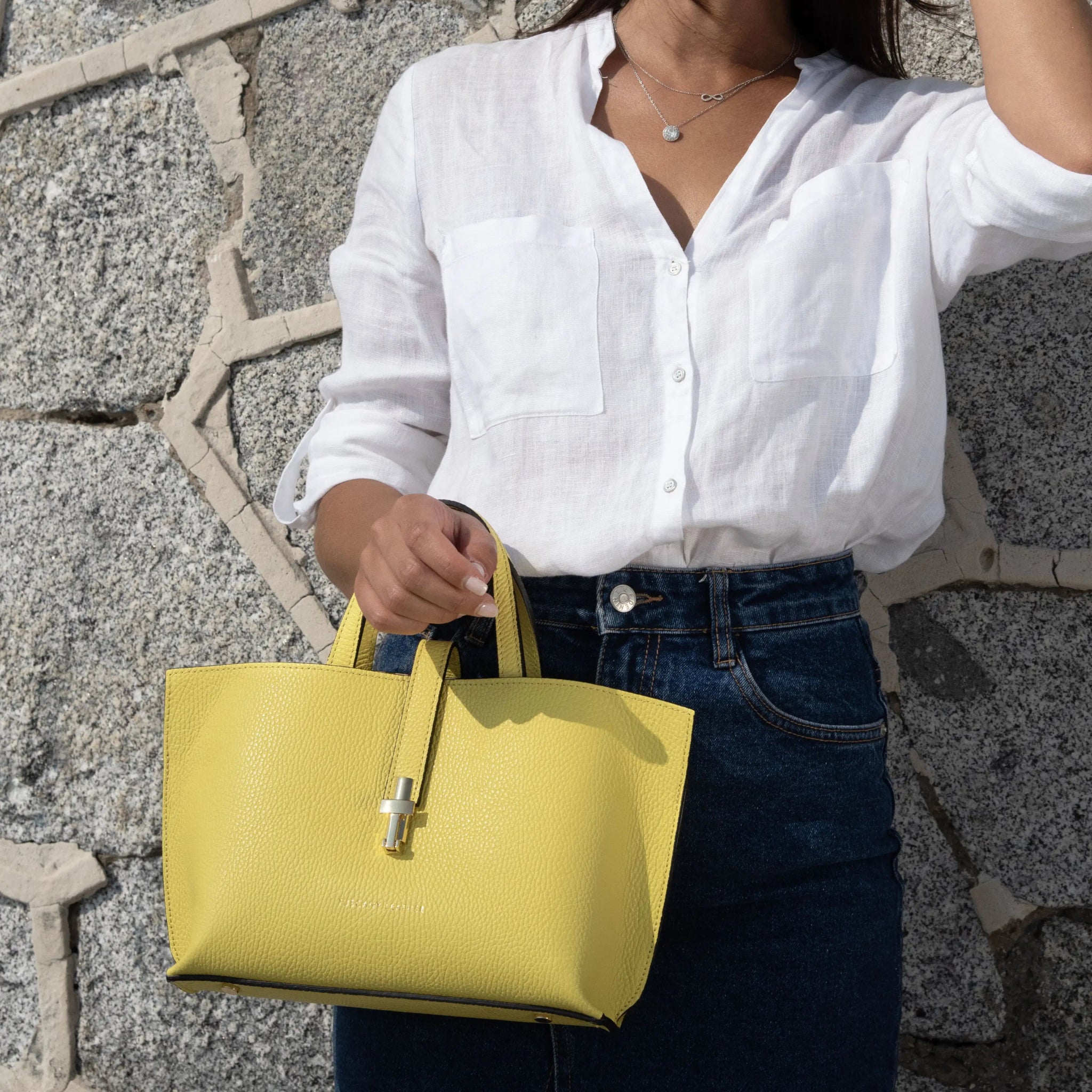 Woman holding a yellow handbag against a stone wall background