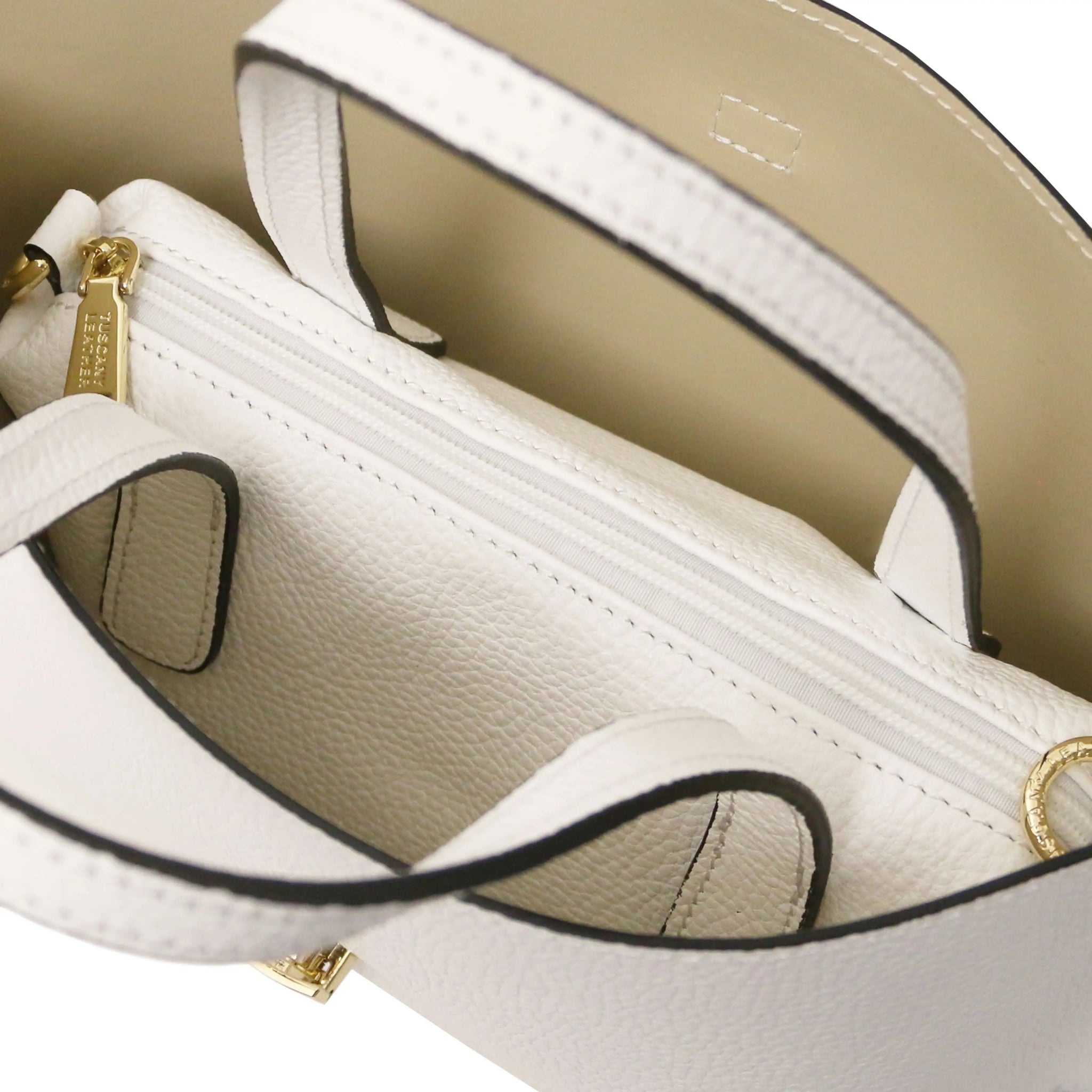 Close-up of a white handbag with beige lining and central zippered compartment