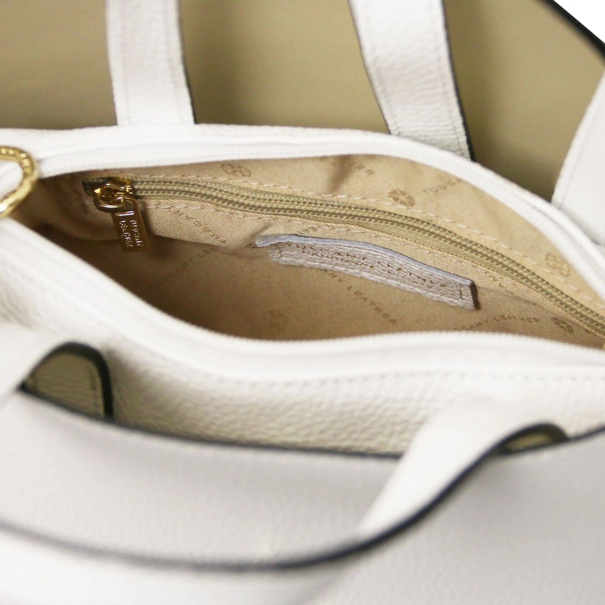 Close-up of a white handbag interior with visible brand logo, beige lining and a zippered pocket
