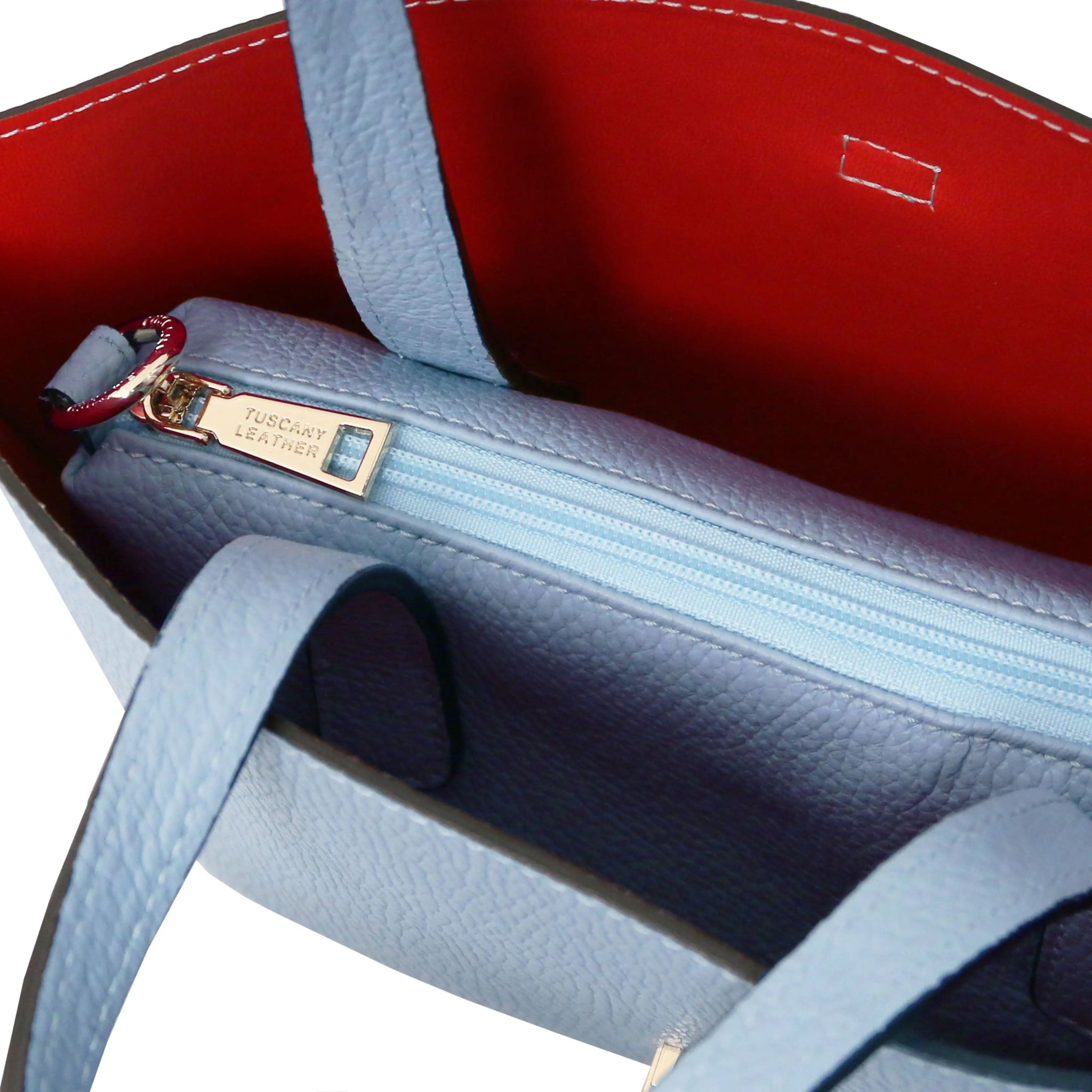 Close-up of a light blue leather handbag with a zippered central compartment and red interior visible.