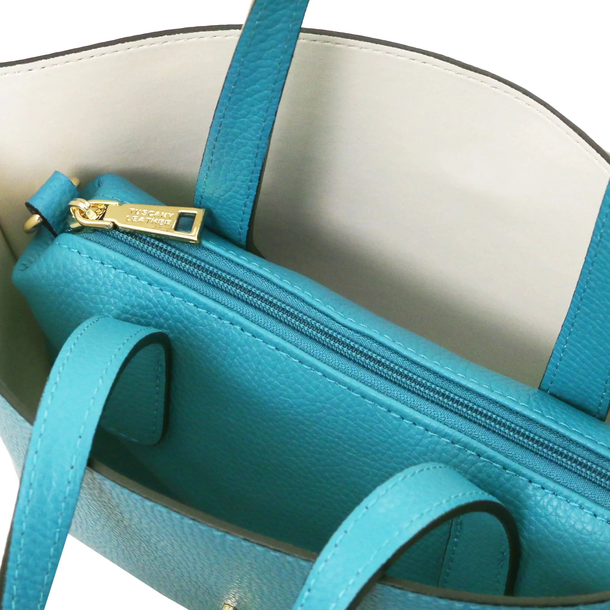Turquoise handbag with beige interior and central zippered compartment on a white background