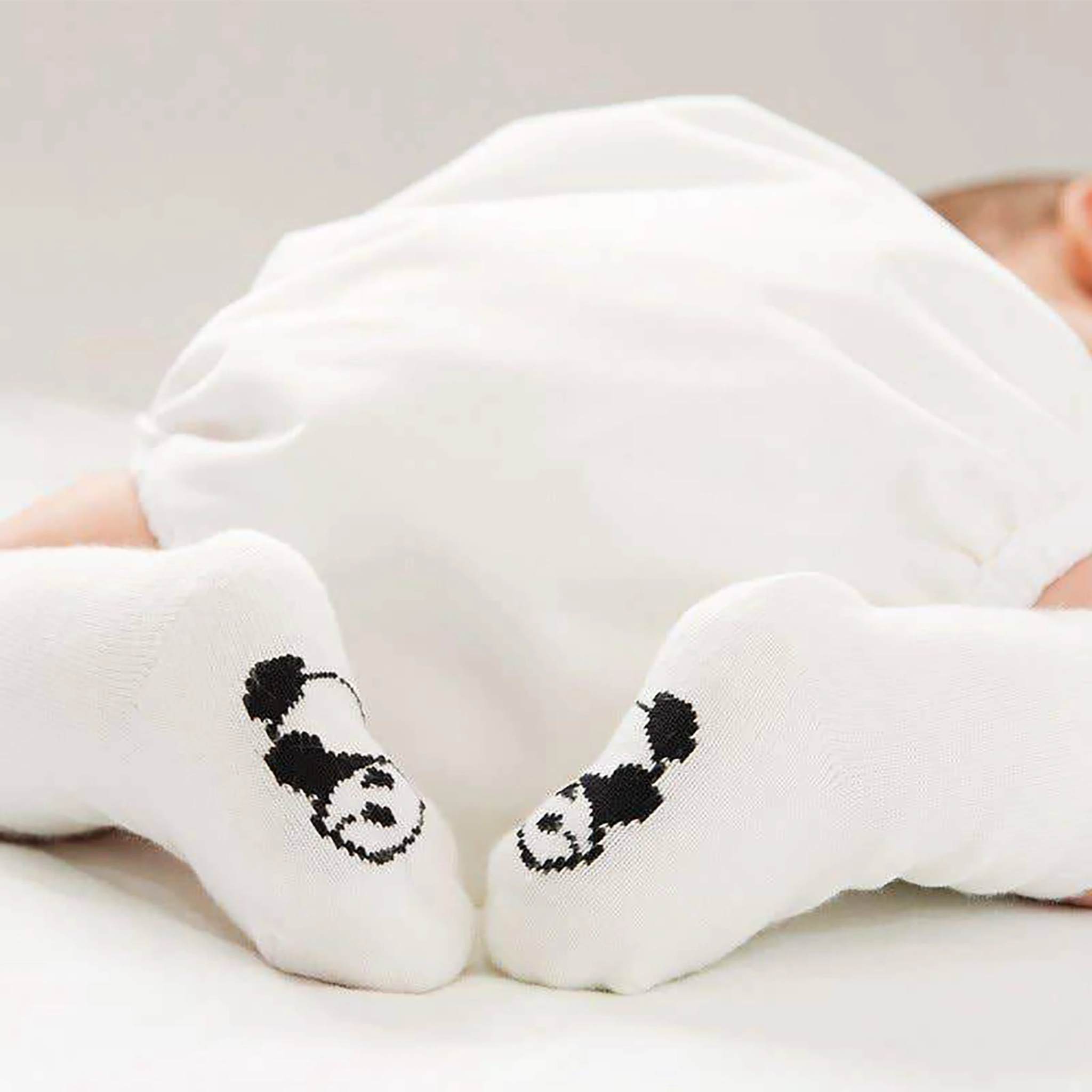 Baby wearing white socks with panda designs on a light background
