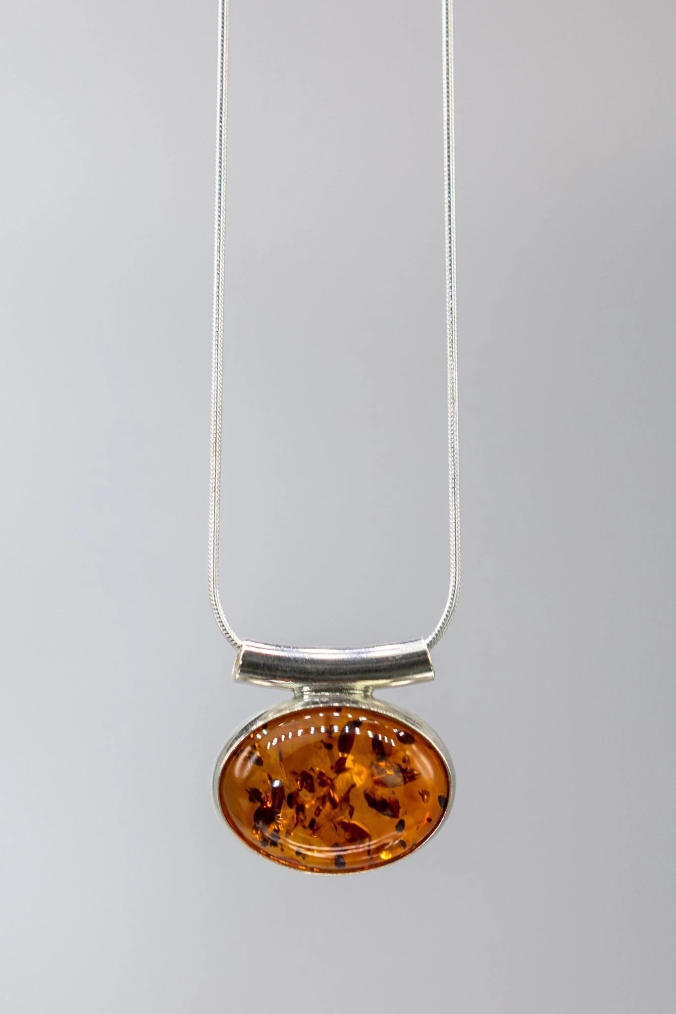 Amber pendant on a silver chain against a gray background