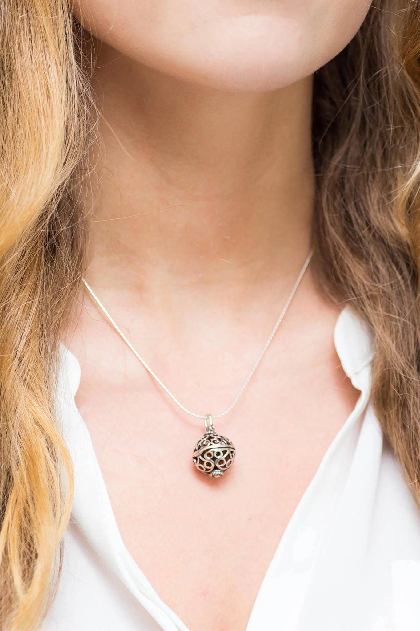 A female model is wearing the Baltic Honey Amber Sterling Silver Filigree Locket Necklace