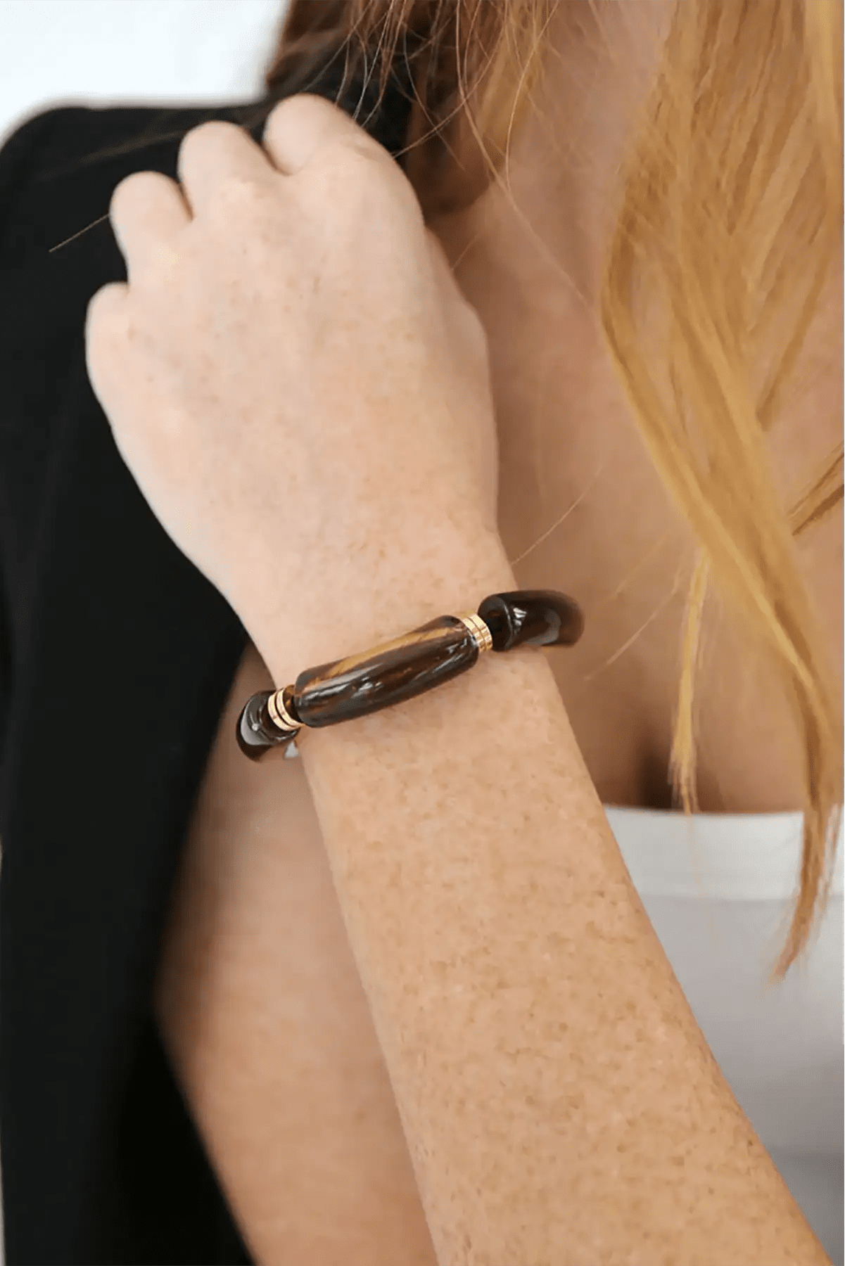 Close-up of a person wearing a brown bracelet on a plain background