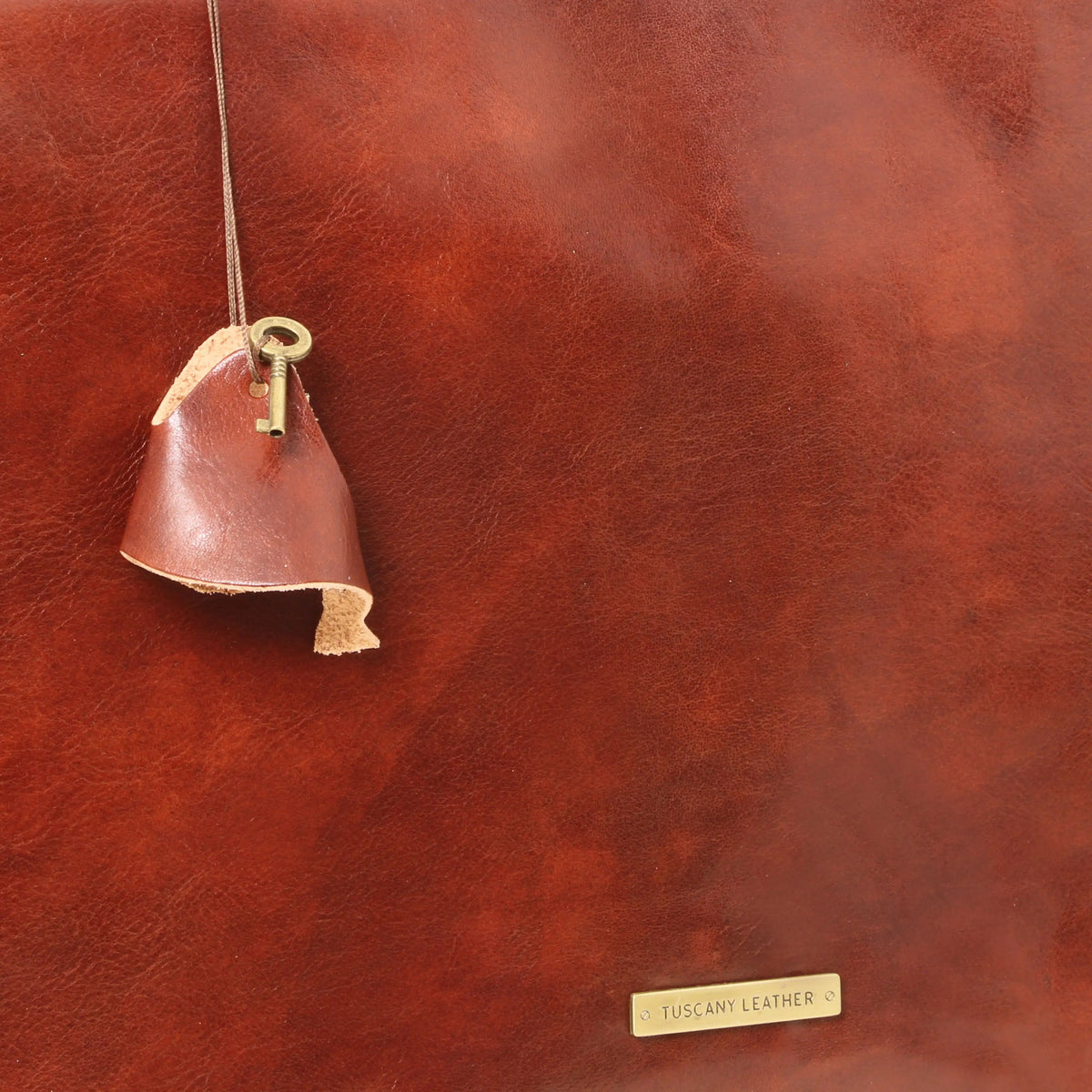 Brown leather close up of front of Mantoya brown bag showing gold metal Tuscany Leather branding