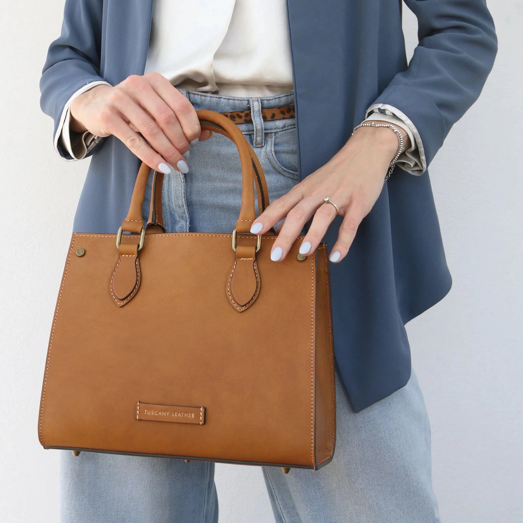 Woman wearing a blue jacket holding the Dama Leather Handbag in natural