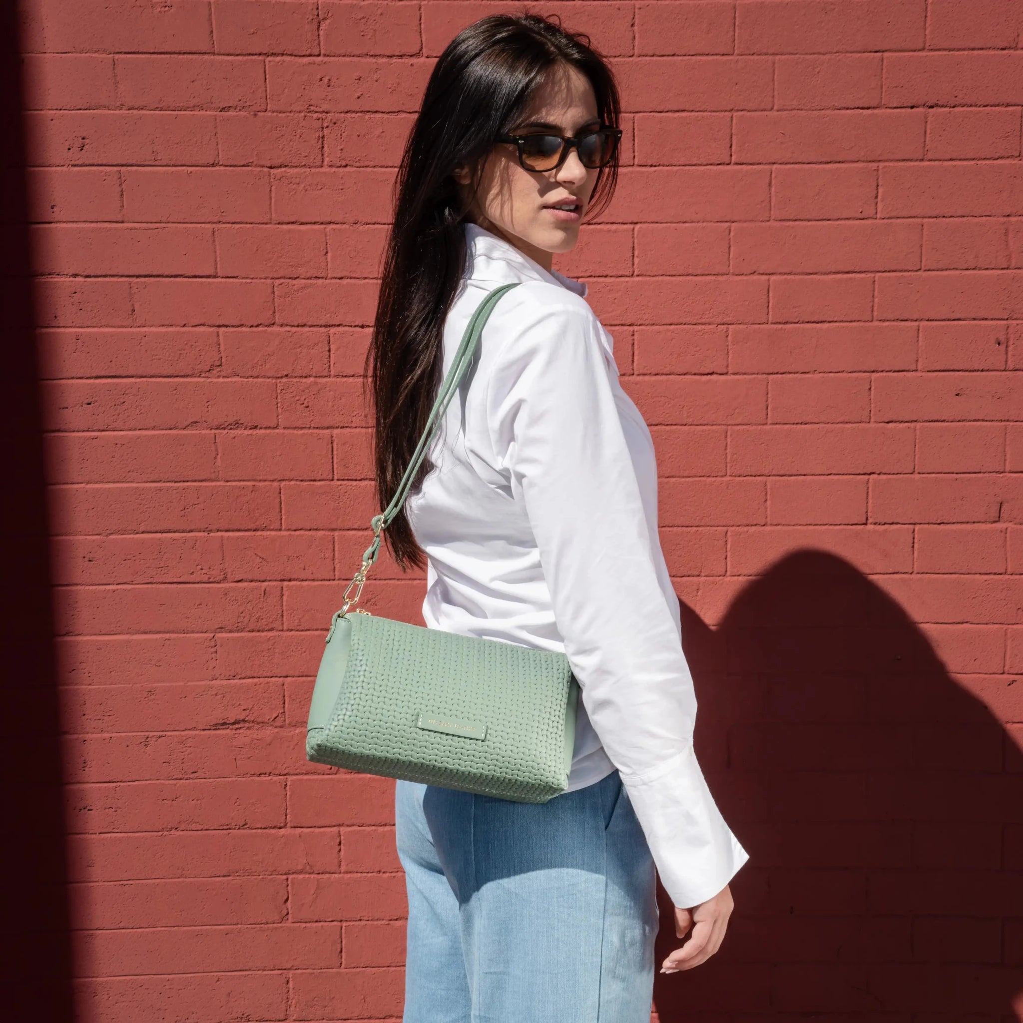 A woma wearing a white blouse carrying the Dedalo Shoulder Bag in Green 