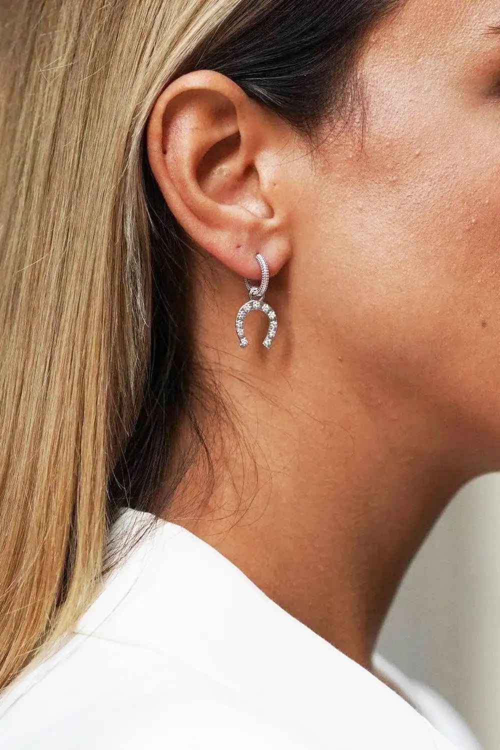 Close-up of a person wearing a silver earring with a horseshoe design.