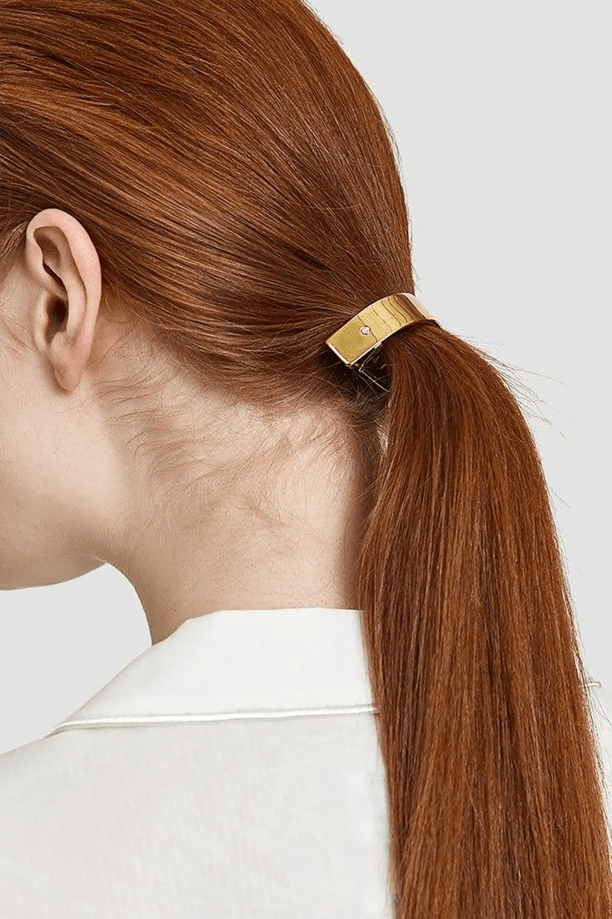 Woman with red hair tied in a ponytail using a gold barrette against a white background