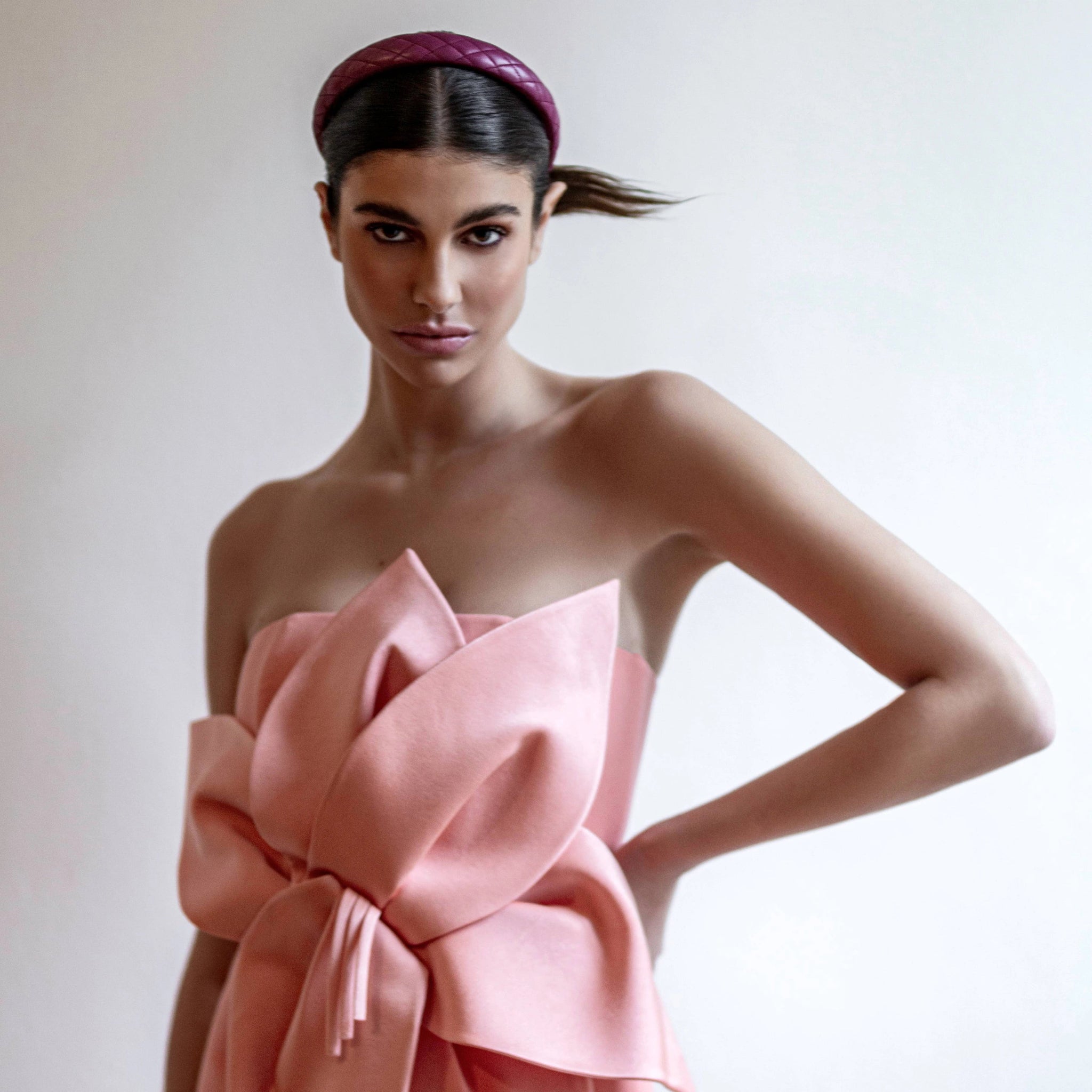 Woman wearing a pink strapless dress with a large bow on a plain background