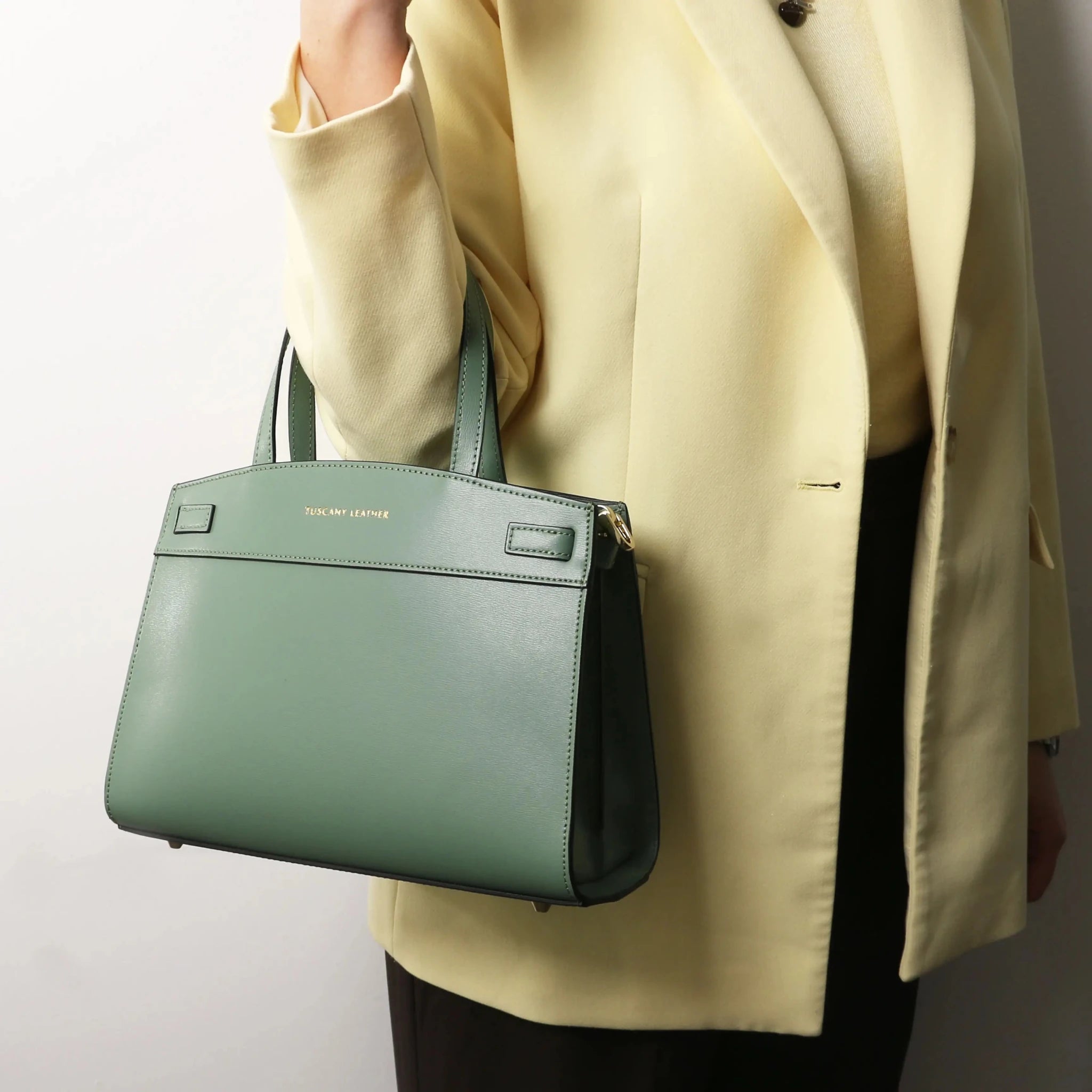 A woman is holding the Musa Italian Smooth Leather Tote Bag in mint green by her elbow