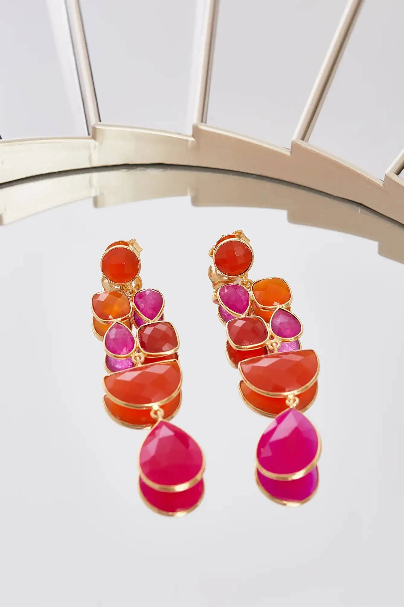 Colorful earrings with pink and orange gemstones on a mirrored background